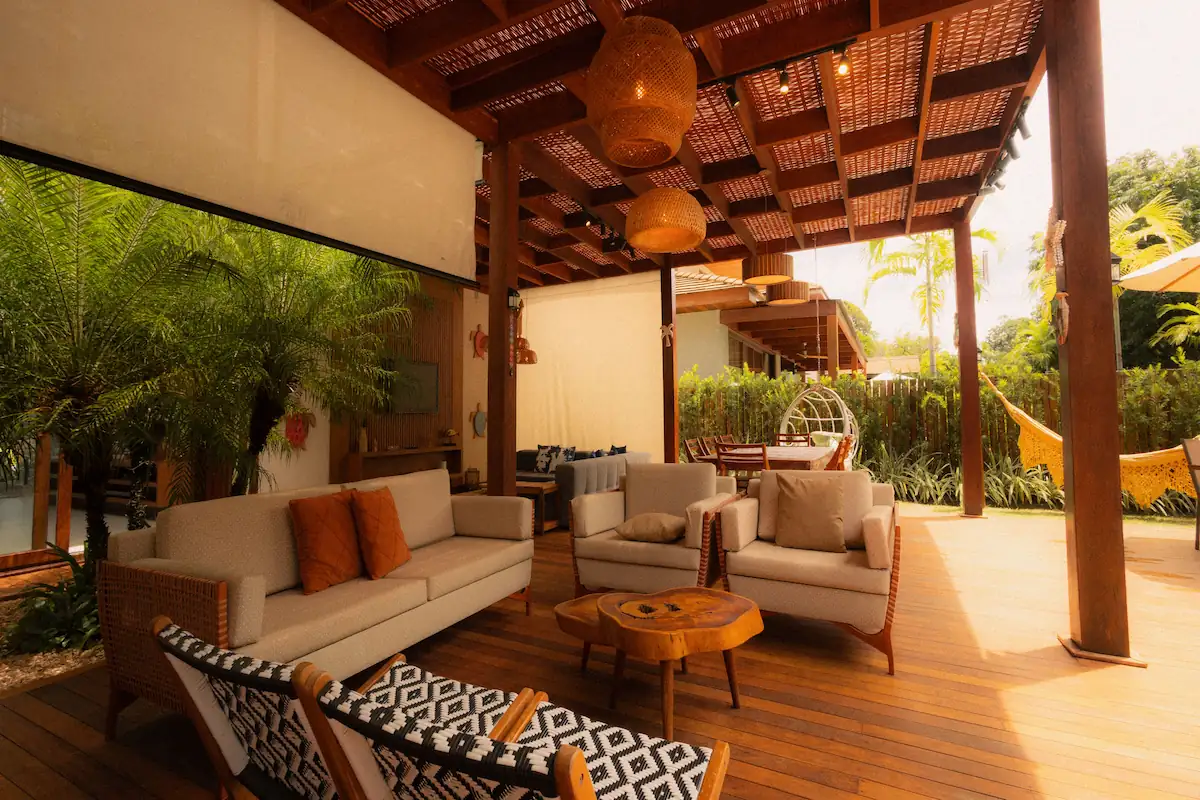Covered patio with warm wood decking, woven pendant lights, cushioned seating, and tropical greenery.
