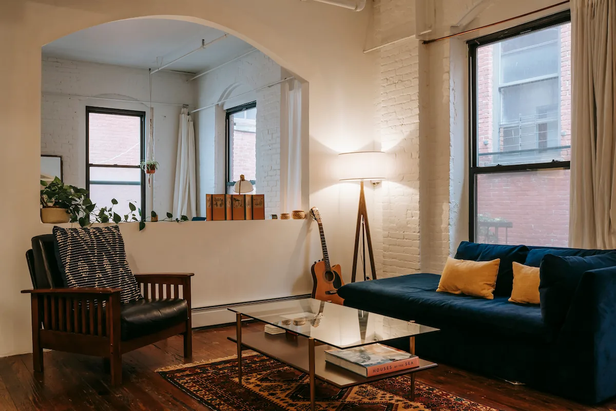Cozy living room with a navy sofa, warm floor lamp, houseplants, and an arched doorway.
